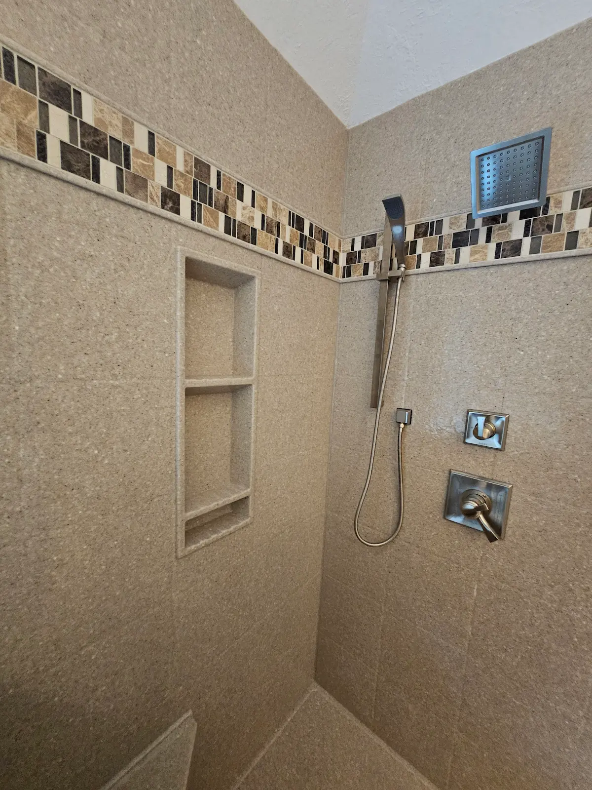 Custom solid stone panel corner shower with mosaic tile border and custom glass enclosure